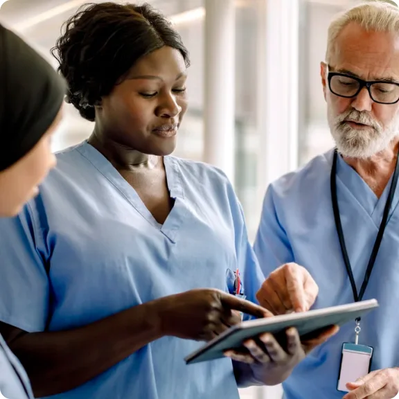 Tres profesionales de la salud están mirando una tableta y discutiéndola.